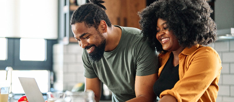 Jeune couple souriant regardant un ordinateur portable ensemble dans la cuisine