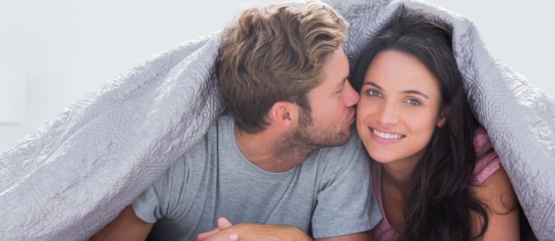 Handsome Man Kissing His Wife Under the Duvet in Bed