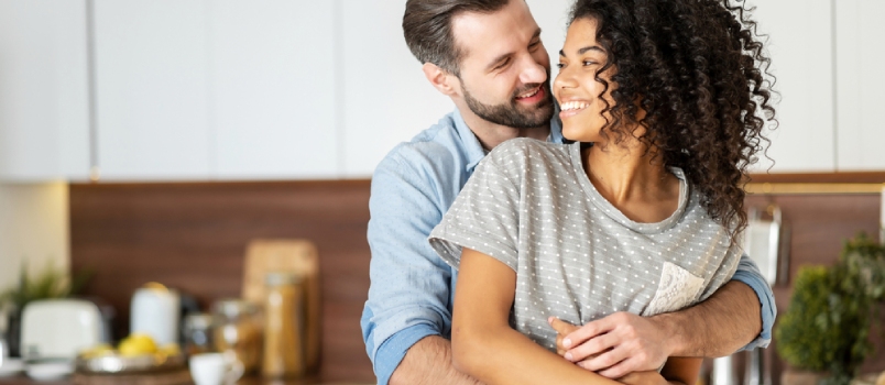 Smiling Man Hugging From Behind Charming African American Woman, Two People Standing and Joyfully Looking at Each Other