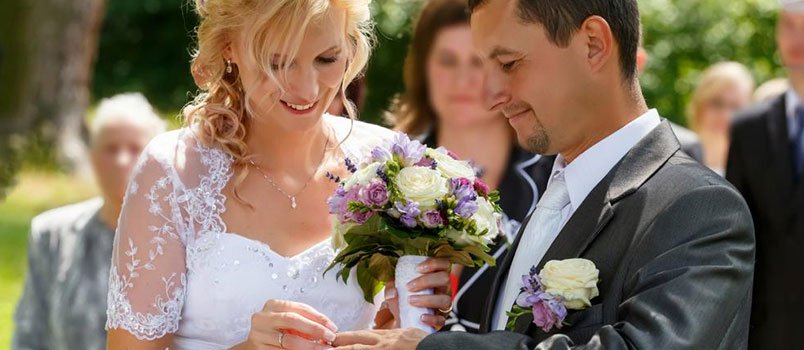 Woman putting wedding ring on man's finger in a wedding ceremony