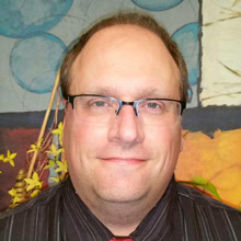 Sad Man Sitting Alone On Kitchen's Table While Blurred Women Standing Behind In Quarreling Position