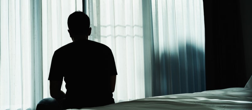 Sad man sitting on bed looking outside of window