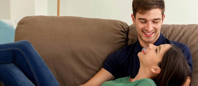 Women Lying On Man Lap On Sofa At Home Smiling Together In Love