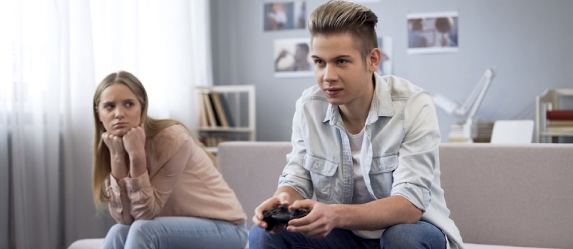 man busy playing video game and woman sitting sadly