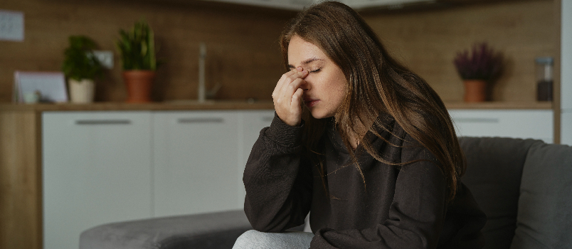 Mujer sentada en el sofá con dolor de cabeza en casa