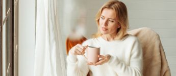 smiling woman sitting with a cup of coffee, looking outside the window
