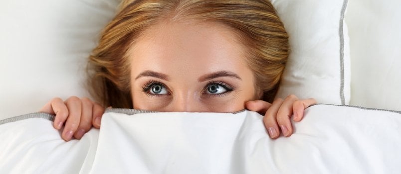 scared woman peeping from blanket