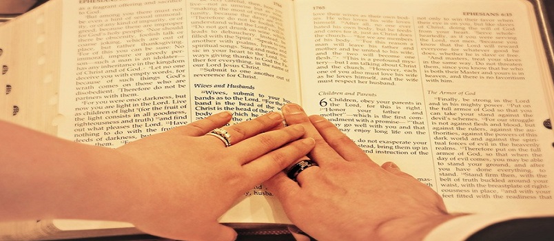 White man and woman with hands placed on the Bible