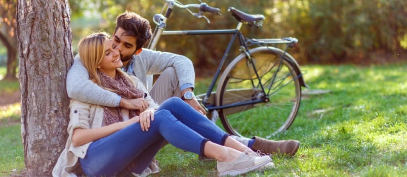 Man kissing woman on cheek while they both sit in nature