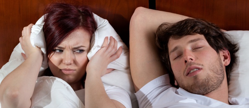 man sleeping and snoring and woman trying to close her ears with pillow