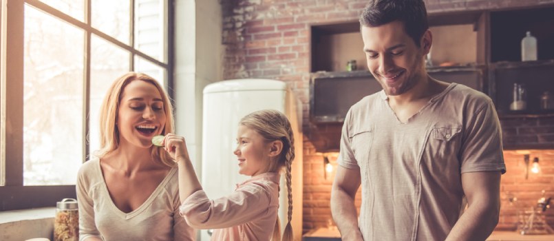 Child feeds mom as she works and dad cooks food