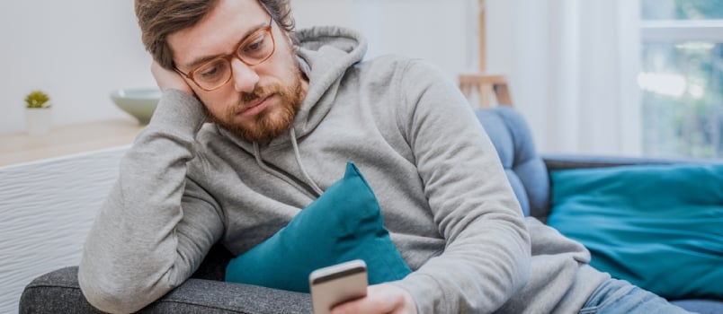 Upset Man Using Mobile Phone Sitting Alone on Sofa At Home