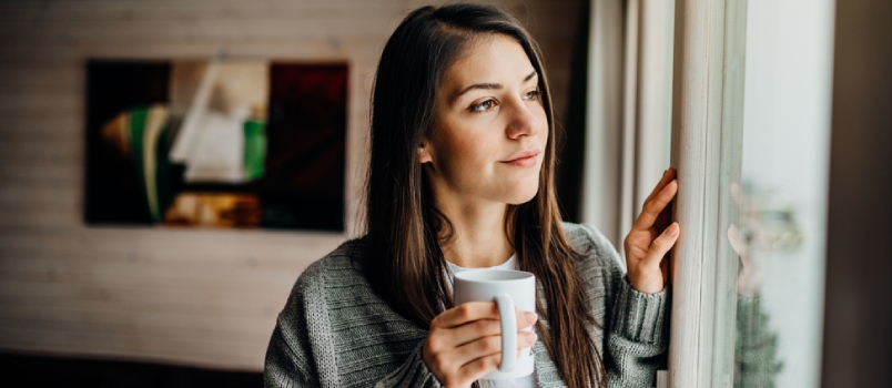 woman driking coffee and staring outside window