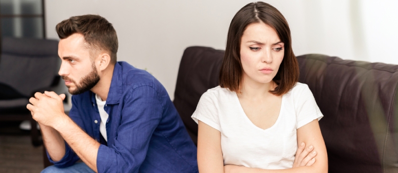 Sad frustrated young couple being in quarrel sitting on sofa in living room and thinking about their problems