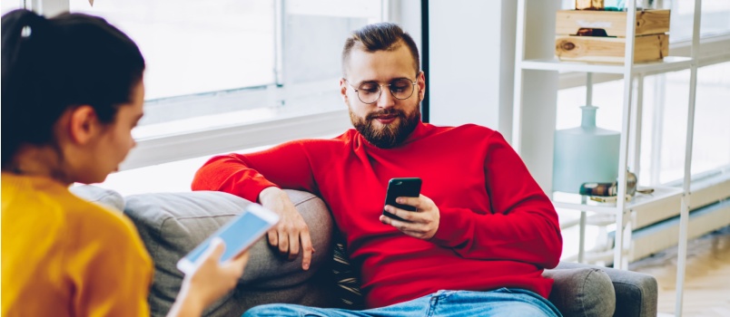 couple sitting on couch using smartphone