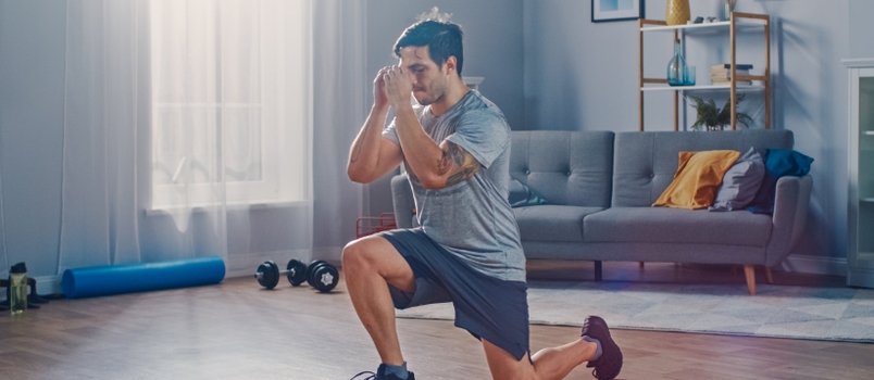 Strong Athletic Fit Man in T-shirt and Shorts is Doing Forward Lunge Exercises at Home