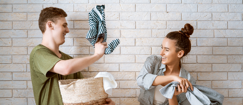 Homme et femme souriants faisant la lessive ensemble à l'intérieur