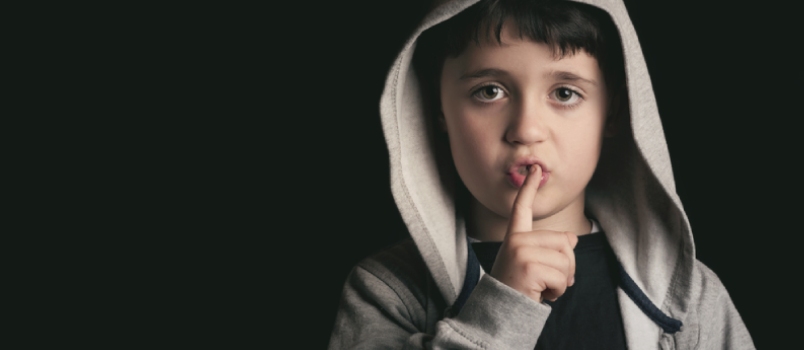 Unusually secretive behavior Little Boy Making Silence Gesture Over Black Background