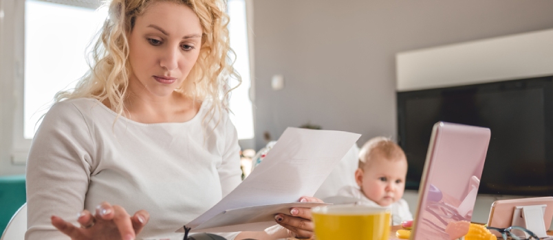 Mother Holding Letter And Using Calculator At Home Office And Taking Care Of Her Baby