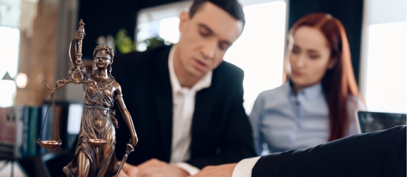 Statue Of Themis Holds Scales Of Justice In Unfocused Background Adult Man And Women At The Lawyer Office