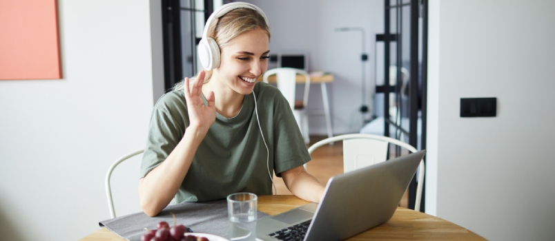 Cheerful Girl In Headphones Waving Her Hand To Friend While Communicating Through Video-chat In Front Of Laptop