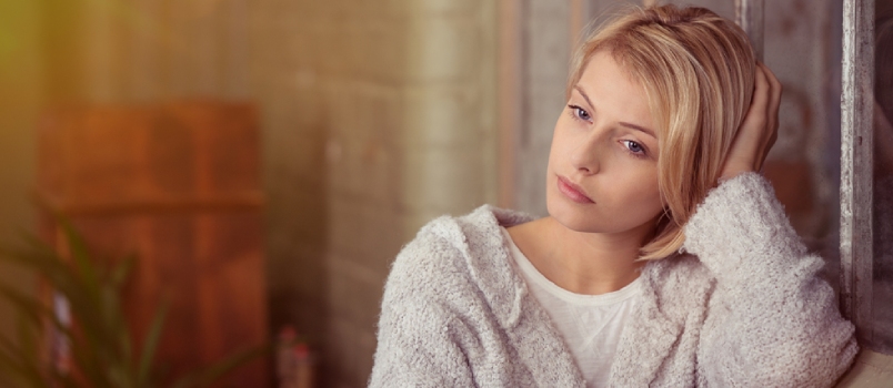 Sad Young Woman Sitting Thinking Resting Her Head On Her Hand On The Back Of The Sofa As She Stares At The Ground With A Serious Expression