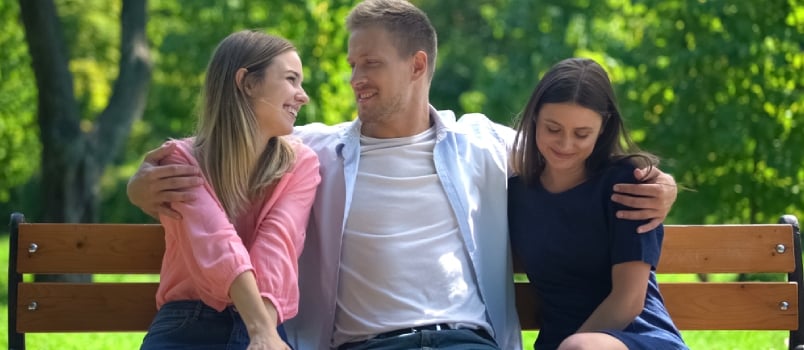 Handsome Man Resting On Bench In Park Hugging Two Attractive Females