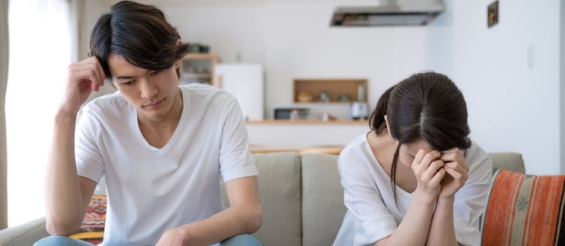 Depressed Couple Sitting Together At Home On Couch While Women Head Down And Crying