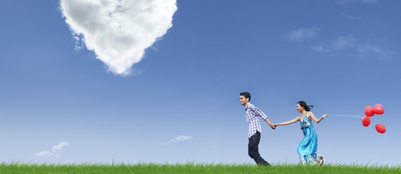 Happy Couple Is Running Together In Green Field While Holding Red Balloons