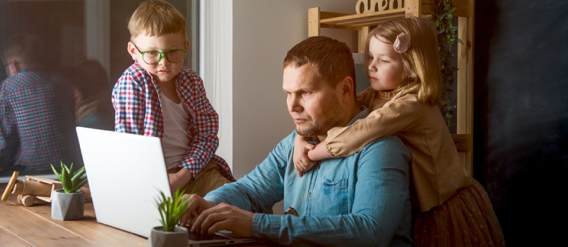 Man Works On Laptop With Children Playing Around Family Together