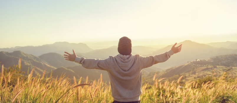 Carefree Happy Man Enjoying Nature On Grass Meadow On Top Of Mountain Cliff With Sunrise