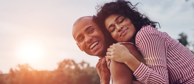Happy Young Couple Embracing And Smiling While Sitting On The Pier Near The Lake
