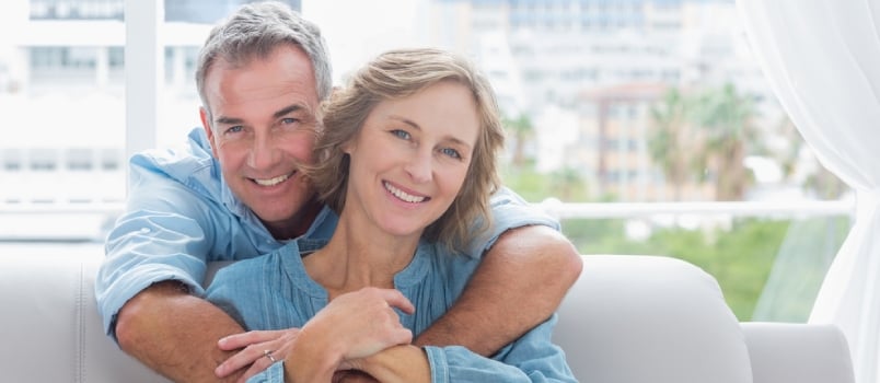 Content Man Hugging His Wife On The Couch Smiling At Camera At Home In The Living Room