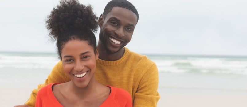 Portrait Of Diverse Couple Standing At Beach They Are Smiling And Looking At Camera