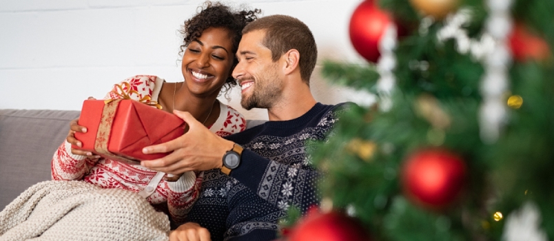 Romantic Multiethnic Couple Exchanging Gifts Near Decorated Christmas Tree