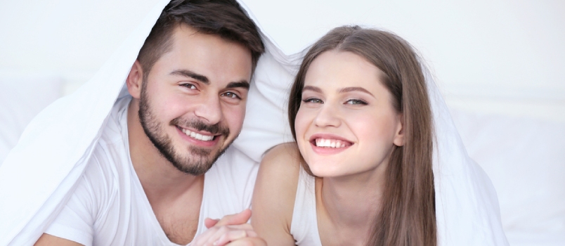 Cute Young Couple Lying On Bed Under Sheet