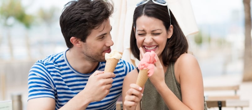 Laughing couple eating ice cream cones as they sit at an open-air restaurant over a cup of coffee in the summer sunshine