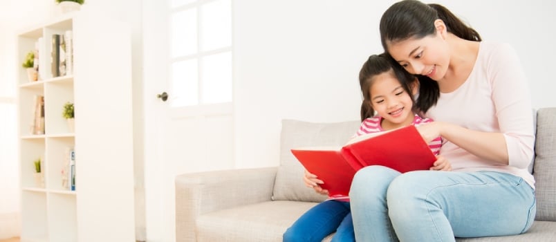 Happy Asian Chinese Mother And Little Daughter Girl Reading A Book In The Morning Together In The Living Room At Home