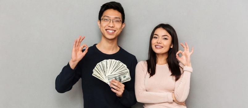 Young Asian Loving Couple Standing Isolated Over Grey Wall Background Holding Money Showing Okay Gesture