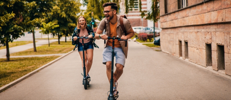 Young Couple On Vacation Having Fun Driving Electric Scooter Through The City