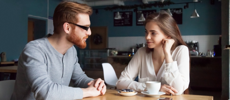 Millennial Red-haired Man Approaching Beautiful Young Girl Enjoying Coffee And Dessert In Café, Interested Young Guy Get Acquainted With Pretty Female
