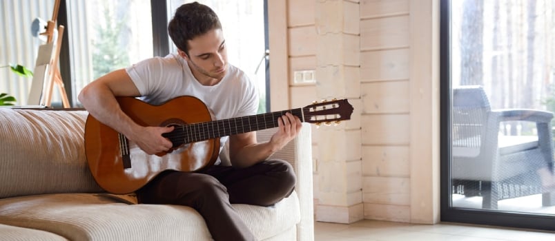 Jolie jeune femme jouant de la guitare assise sur le canapé dans le salon lumineux