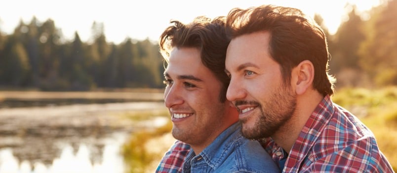 Happy gay couple sitting near river side