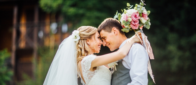 Couple In Love Looks One-on-one Bridge Holding Flowers In Hand