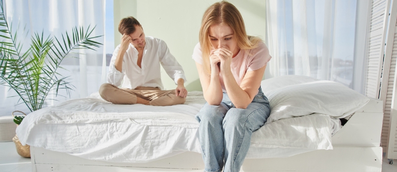 Young Couple Quarreled And Sit Upset On The Bed. The Concept Of Relationship Problems