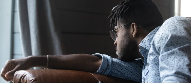 Upset Young African American Male Sit On Sofa At Home Look In Distance Mourning Missing