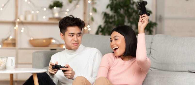 Korean Young Couple Playing Video Games Together, Asian Husband Losing Videogame To Wife Sitting In Living Room At Home