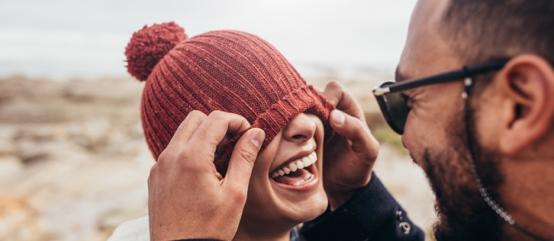 Loving Couple Having Fun Outdoors. Man Covering Eyes Of Woman With Cap