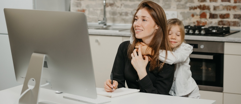 A Young Mother Is Working Remotely At Home While A Daughter Is Hugging Her Behind