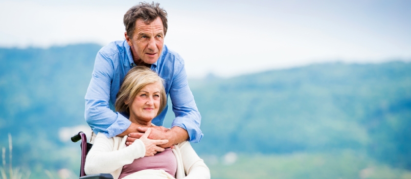 Senior Man With Woman In Wheelchair Outside In Nature